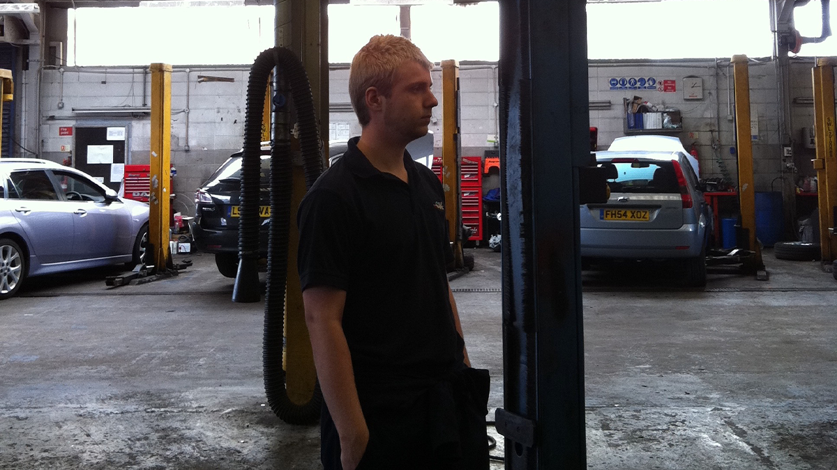 The sad and youthful looking author of this article back when he was a vehicle technician. Stood in a workshop among two poster ramps.